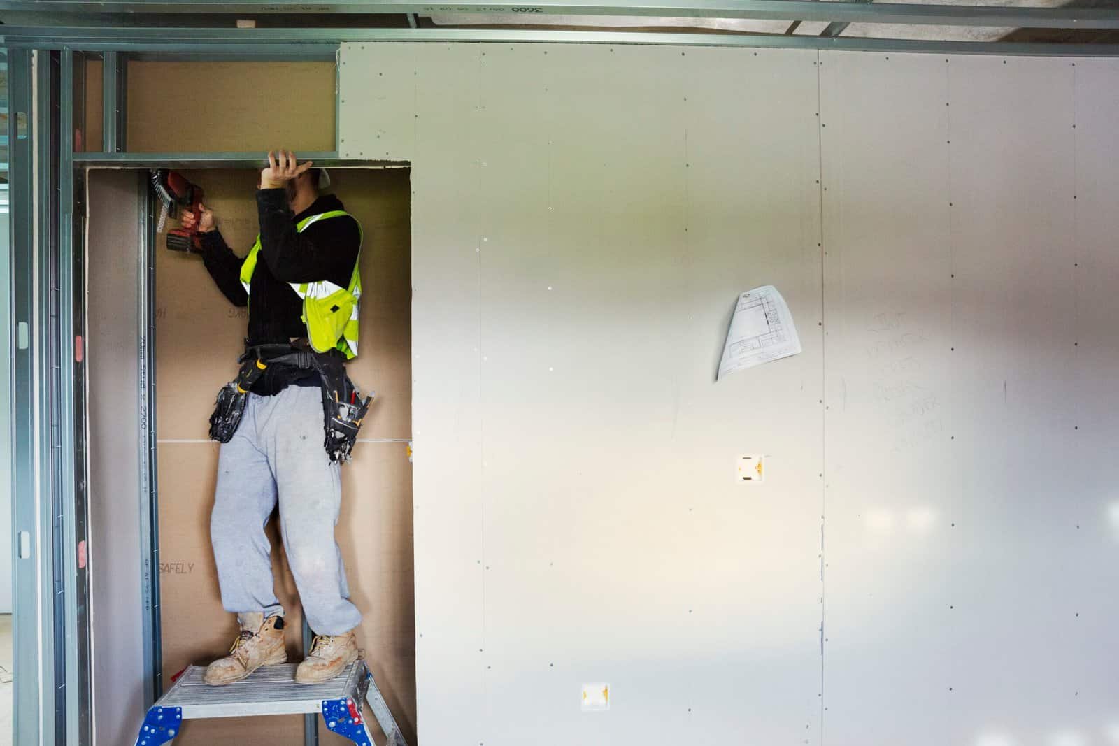 Skilled drywall installer working on wall installation at construction site.